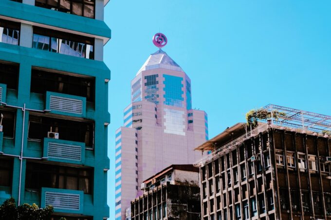 Striking architectural contrast showing a small, unique building standing proudly next to a towering modern skyscraper, sy...